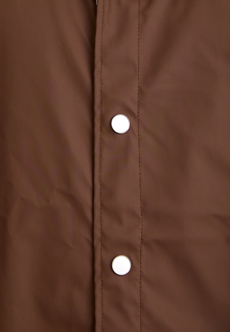 Brown padded jacket featuring a smooth texture, metallic snap buttons, and prominent stitching along the fabric.