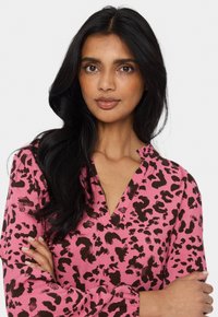 Rosa blus med ett leopardsmönster i brunt, med v-ringning och långa ärmar, tillverkad av ett lätt tyg.