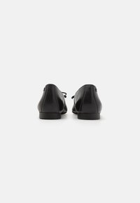 Ballet flats in pelle nera con punta arrotondata, cuciture sottili e tacco basso. Presentano un dettaglio a fiocco nella zona del tacco.