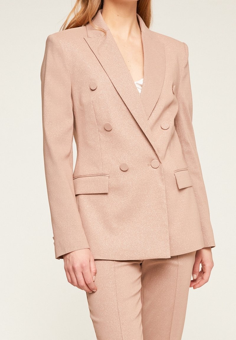 Světle růžový dvouřadý blazer vyrobený z třpytivého materiálu, s kulatými knoflíky, klopami a strnulými rameny. Elegantní střih.