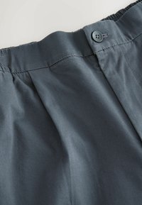 A szürke vászonshorts sima elejű, rugalmas derekú és gombos részletű. Az anyaga sima, finom redőkkel.