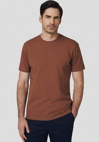 Brązowa koszulka z krótkim rękawem, wykonana z bawełny, z klasycznym okrągłym dekoltem i gładką fakturą, połączona z ciemnoniebieskimi spodniami.