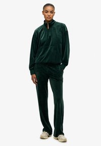 Donkergroene velours trainingsoutfit met een half-zip pullover met een voorzak, en bijpassende broek met een elastische tailleband en subtiele details.