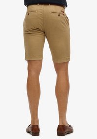 Khaki shorts met een rechte snit, twee achterzakken en subtiele stikdetails, gedragen met bruine schoenen. Het materiaal lijkt lichtgewicht en duurzaam.