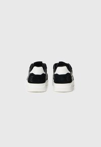 Mustvalge sneakerid, nähtavad seljaga, valgete taldadega ja musta tähelogoga kontsapoolses osas.