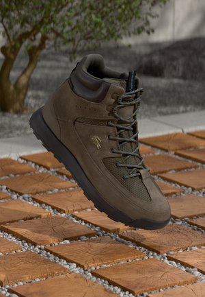 Brown suede hiking boot with mesh accents, padded collar, contrasting blue laces, and a textured rubber sole, set on wooden tiles and gravel.