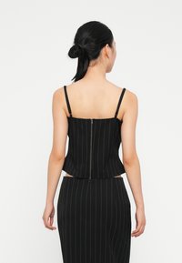 Top corto negro con rayas verticales, tirantes finos y cremallera trasera. La tela parece suave, con un diseño estructurado y una silueta ajustada.