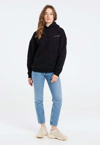 Felpa nera con tasca frontale e coulisse, abbinata a jeans azzurri chiari e sneaker beige. Tessuto morbido con vestibilità comoda.
