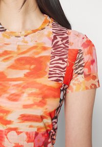 Chemise multicolore à manches courtes présentant un mélange de motifs floraux et animaliers, principalement dans des tons orange, rose et marron, avec un col rond.