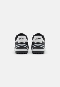 Sorte atletiske sko med hvide detaljer, iøjnefaldende hældesign, tekstureret gummiydersål og mærket "JAKO" bagpå.