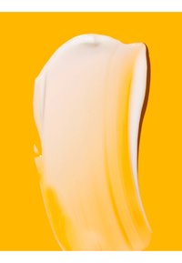 Gładka beżowa smuga kremu o błyszczącej teksturze na jednolitym jasnym pomarańczowym tle.