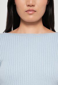 Light blue ribbed knit sweater with a wide neckline, featuring a soft texture and fitted design, highlighting subtle vertical lines.