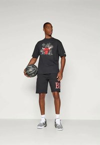 Μαύρη μπλούζα με πολύχρωμο γραφικό σχέδιο, μαύρη βερμούδα με κόκκινο κείμενο "BU" και μπάλα μπάσκετ, φορεμένα με γκρι και λευκά αθλητικά παπούτσια.