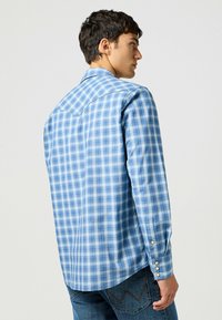 Camicia button-up a quadri blu con colletto classico, maniche lunghe e bottoni in perla. Tessuto morbido con una vestibilità rilassata e orlo arrotondato.