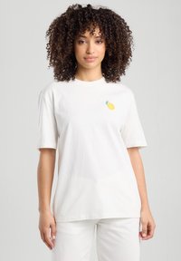 White cotton t-shirt with short sleeves, featuring a small yellow lemon graphic on the left chest area. Smooth texture, relaxed fit.