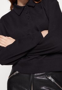 Černá polo mikina s dlouhým rukávem, zapínáním na knoflíky, ribbed manžety a texturovanou látkou, kombinovaná s černými koženými kalhotami se zipy.