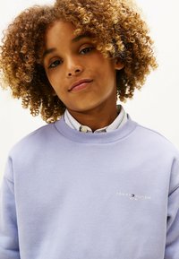 Lyse lilla sweatshirt lavet af bomuldsblanding, med ribbet halsudskæring og lille broderet logo på brystet. Blød struktur og afslappet design.