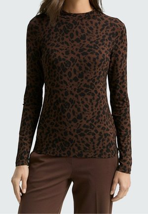 Woman wearing a long-sleeve fitted brown top with black leopard spots and matching brown pants, standing against a plain background.