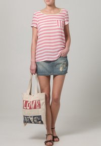 Randig rosa och vit T-shirt med ficka, tillsammans med en denim minikjol. Canvas tote-bag med röd och blå text. Bruna sandaler.