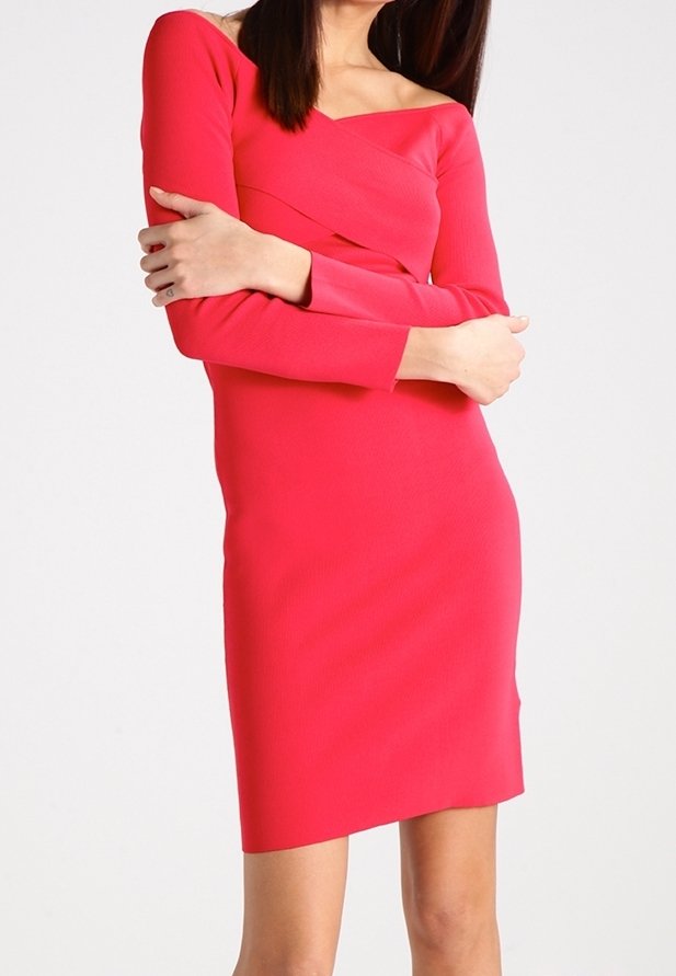 Femme portant une robe longue rouge vif ajustée avec des manches longues et un décolleté asymétrique, debout, les bras croisés devant un fond uni.