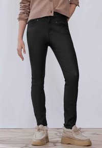 Jeans ajustados negros hechos de una tela suave, con una cintura de media altura y diseño de cinco bolsillos, combinados con zapatos beige con borde de piel de oveja.