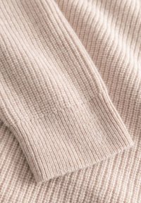 Hellrosa gestrickter Pulloverstoff mit geripptem Muster, der ein umgeschlagenes Bündchen und ein weiches, warmes Erscheinungsbild aufweist.