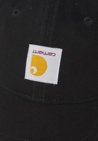 Czarna czapka z teksturowanej tkaniny. Posiada białą metkę z żółtym i pomarańczowym wzorem, na której widnieje nazwa marki "Carhartt."