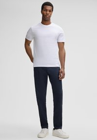 Witte katoenen t-shirt gecombineerd met donkerblauwe broek. Het model draagt witte sneakers, wat een klassieke, casual outfit met een schoon ontwerp laat zien.