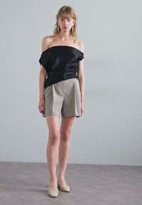 Černý saténový top s odhalenými rameny, spárovaný se světlými šedými upravenými šortkami. Krátký střih a tkané béžové boty dotvářejí vzhled.