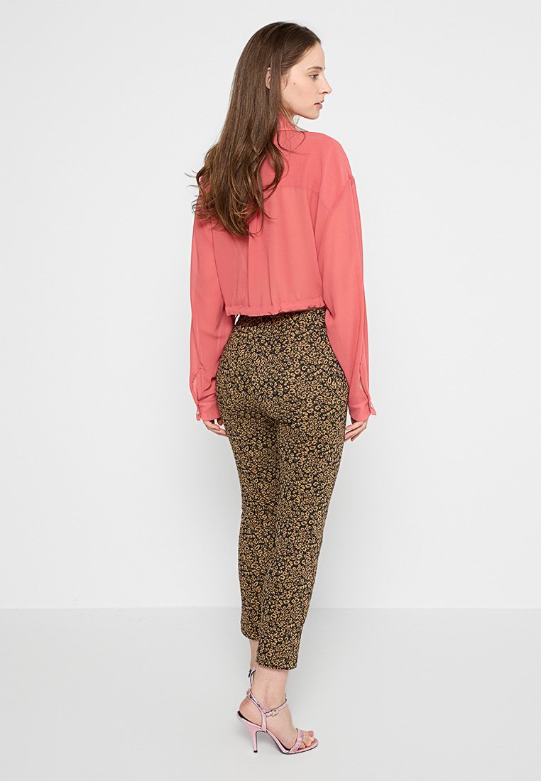 Rosa kurze Bluse und braune Hosen mit floralen Mustern, kombiniert mit rosa Riemchen-High Heels. Weiches Material, taillierte Passform und Knöchellänge.