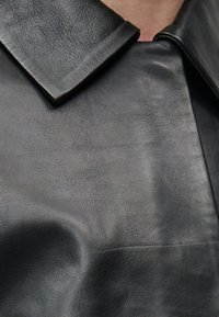 Κοντινό πλάνο ενός ατόμου που φορά μαύρο δερμάτινο μπουφάν με γιακά και εμφανή υφή στο υλικό.