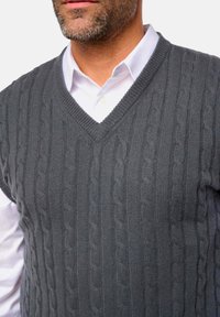 Dunkelgrauer, kabelgestrickter Sweater-Weste mit V-Ausschnitt, übereinander getragen über einem weißen Hemd mit Kragen. Verfügt über ein strukturiertes Muster und gerippte Abschlüsse.