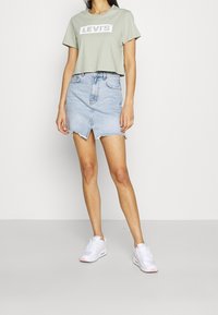 Ljusgrön kortärmad t-shirt med vit Levi's-logotyp, tillsammans med en ljusblå denimkjol med fransad nederkant och framficka. Vita sneakers.