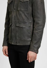 Lederjacke in Dunkelgrau mit Reißverschluss vorne, vier Fronttaschen und sichtbaren Nähten für eine strukturierte Optik.