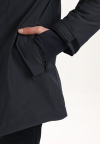 Giacca impermeabile blu navy con tasca laterale con zip, polsini regolabili e texture liscia. Progettata per un uso funzionale all'aperto.