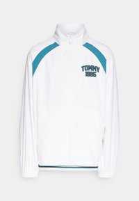 Bílá zipová bunda s tyrkysovými ramenními akcenty, elastickými manžetami a textem "TOMMY 1985" na levé straně hrudi.