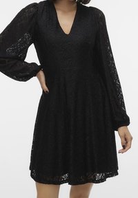 Svart spetsklänning med v-ringning, långa puffärmar och utsvängd kjol. Invecklat blommönster genom hela tyget.