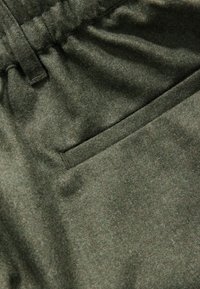 Tissu en laine vert avec une texture douce, featuring une taille cousue et une petite poche rectangulaire.
