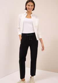 Zwarte, comfortabel zittende broek met een elastische tailleband en koord, gecombineerd met een wit tanktop en een lichtgebroken overhemd.