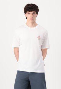Camiseta blanca de algodón con cuello redondo, mangas cortas y un pequeño diseño bordado en un color claro en el lado izquierdo del pecho.