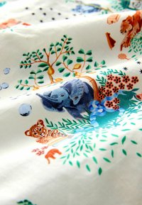 Blauwe olifant en tijgerwelp illustraties tussen groene bladeren, oranje bloemen en bruine takken op witte stof.
