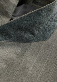 Veste grise à fines rayures sur mesure montrant un gros plan du col en velours doux gris foncé et de la texture lisse du tissu.
