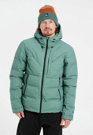 Chaqueta aislante verde menta con cierre de cremallera, capucha ajustable, múltiples bolsillos con cremallera y acentos en negro. Usada con un gorro multicolor.