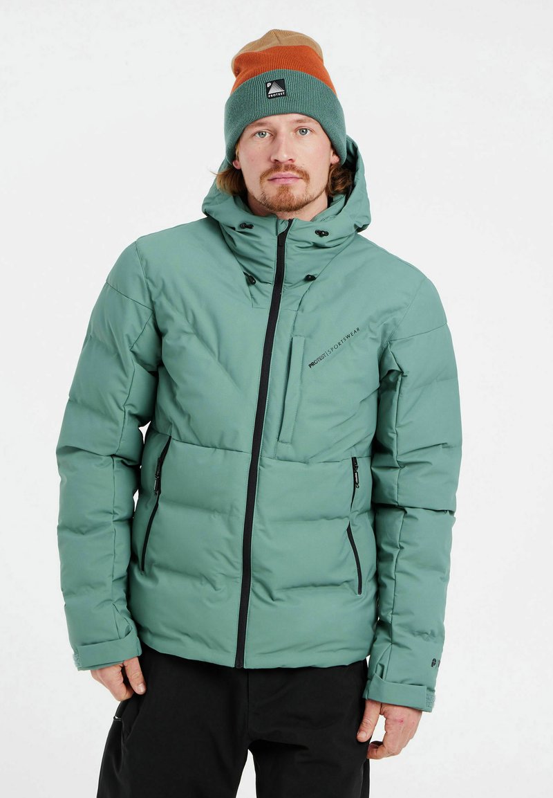 Chaqueta aislante verde menta con cierre de cremallera, capucha ajustable, múltiples bolsillos con cremallera y acentos en negro. Usada con un gorro multicolor.