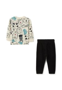 Langärmliges Shirt mit einem beigen Hintergrund und Tiermustern in Schwarz und Türkis; kombiniert mit schwarzen Jogginghosen mit elastischem Bund.