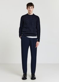 Marineblauer Strickpullover mit Rundhalsausschnitt, kombiniert mit maßgeschneiderten marineblauen Hosen und schwarzen Stiefeletten, vor neutralem Hintergrund.