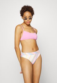 Top de bikini rosa com alças finas, combinado com um fundo de cintura alta em listras multicoloridas, apresentando tons pastel e um design envolvente.