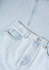 Jean en denim bleu clair avec un design classique à cinq poches. Dispose d'une fermeture à bouton et de détails de couture discrets. Texture lisse.