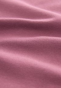 Ružová textília s textúrovaným povrchom, s jemným vzorom. Materiál vyzerá hladko so mäkkými záhybmi a jemnými vlnami.