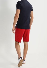 Tenue masculine comprenant un polo bleu marine et un short rouge. Le polo a un col classique, et le short est en coton avec des poches latérales.